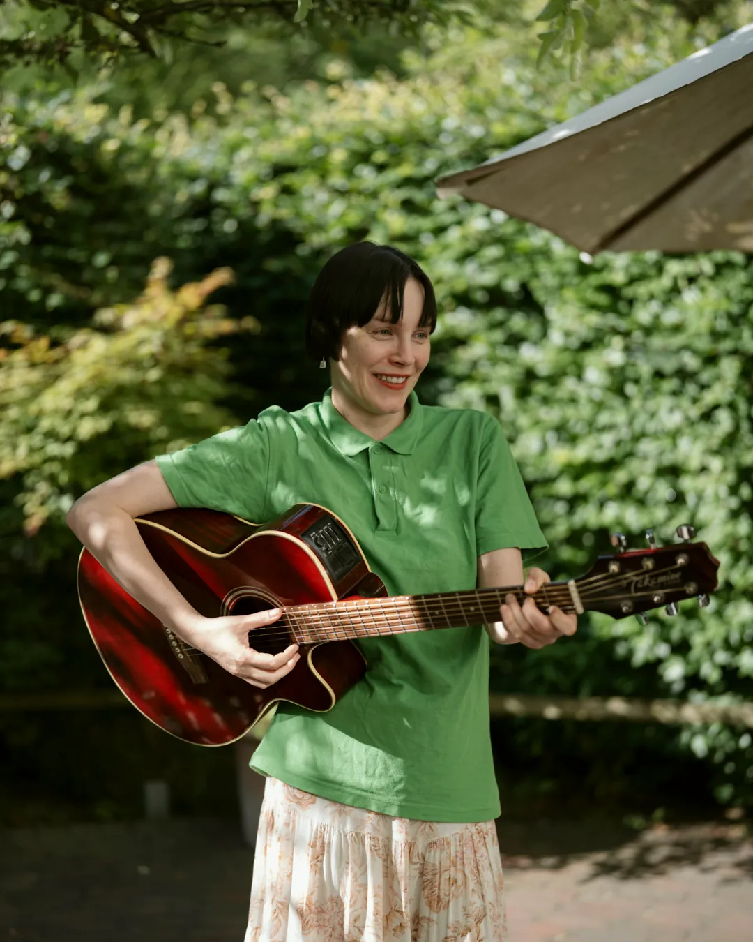 Therapeutin mit einer Gitarre im Garten einer Pflegeeinrichtung, sie lächelt